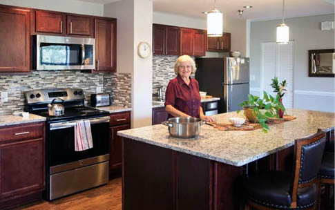 A woman is standing in a kitchen with a marble counter top. Description generated by AI
